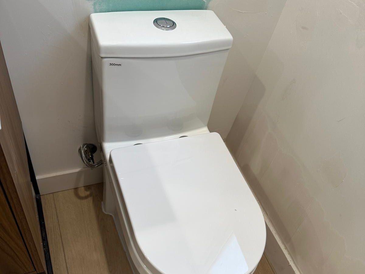 A new white one-piece toilet with a push-button flush, set against a white wall on a light wood floor